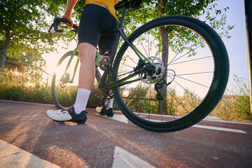 Cyclist walking bicycle along pathway during sunset in urban setting