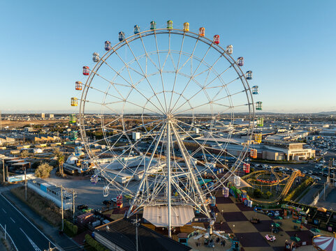 Aerial view of a giant Ferris wheel standing tall against the backdrop of a city, its colorful cars a vibrant contrast to the urban landscape, Osaka, Japan.