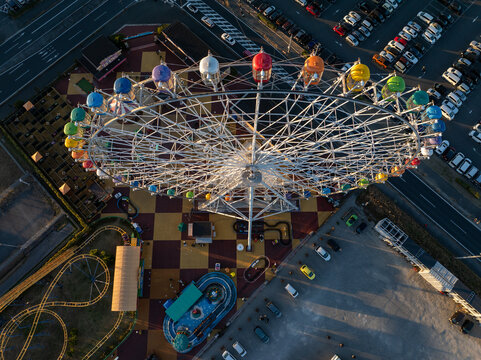 Aerial view of a colorful Ferris wheel and miniature roller coaster contrasting with the checkerboard ground and parked cars, Osaka, Japan.
