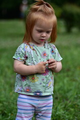Red-haired toddler in unicorn shirt and striped leggings stands on grassy area near playground...
