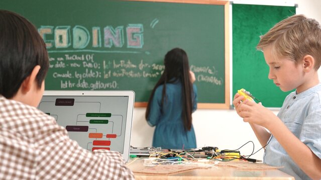 Asian boy coding program while caucasian friend fixing electric board at STEM class. Energetic student standing blackboard while writing coding engineering prompt and programing AI software. Pedagogy. - Powered by Adobe