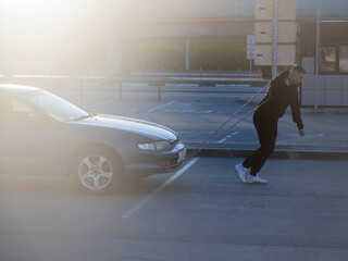 Caucasian man pulling a car with a rope. 