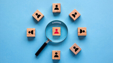 Magnifying glass highlights a unique person among many on wooden blocks, symbolizing talent search and selection for business success.