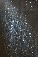 A detailed macro shot of a shower glass pane shows a captivating texture of both dried mineral deposits and fresh water drops.