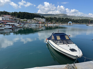 Coastal village in Greece showcases tranquil harbor with boats gently bobbing on calm waters against backdrop of lush hills and vibrant sky, inviting visitors to enjoy seaside charm