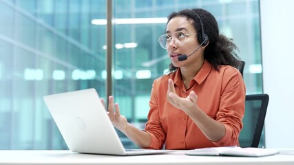 Confident african american businesswoman in wireless headset talking on video call conference using a laptop sitting in office. Female coach speaks remotely, communicates at online meeting, training - Powered by Adobe