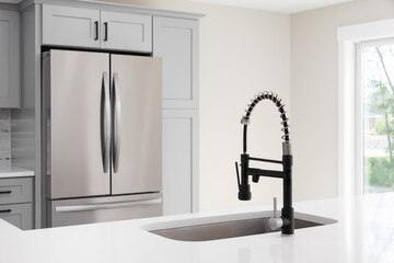 A kitchen faucet detail with a black and stainless steel faucet, white marble countertop, and grey...