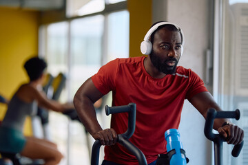 Determined black athlete cycling during spinning class in gym.
