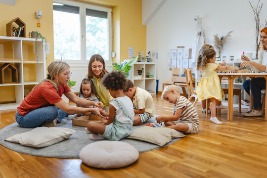 Two preschool teachers with children sitting on floor, engaging in collaborative early learning activity in bright classroom
