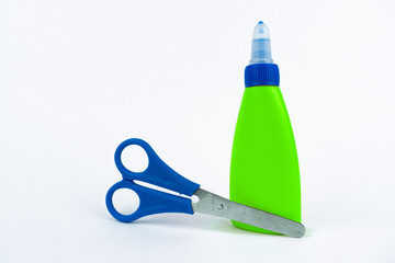 Green glue bottle with blue cap next to blue scissors with metal blade on a clean white background. concept of school supplies or creative work.