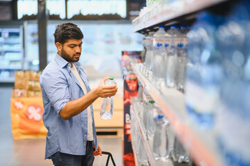Young indian man choosing bottled water in supermarket
