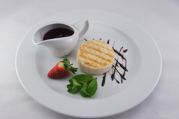 Grilled Camembert cheese served on a white plate with berry jam, strawberries and mint.