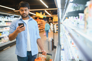 Indian man using smartphone while shopping in supermarket