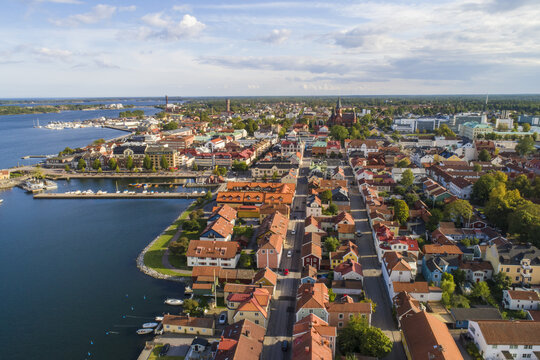 Aerial view of red-roofed buildings meet the shimmering blue harbor, framed by lush greenery and the distant archipelago, Vastervik, Kalmar County, Sweden.