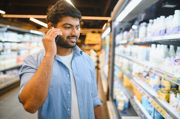 Indian man choosing dairy products while talking on phone in supermarket