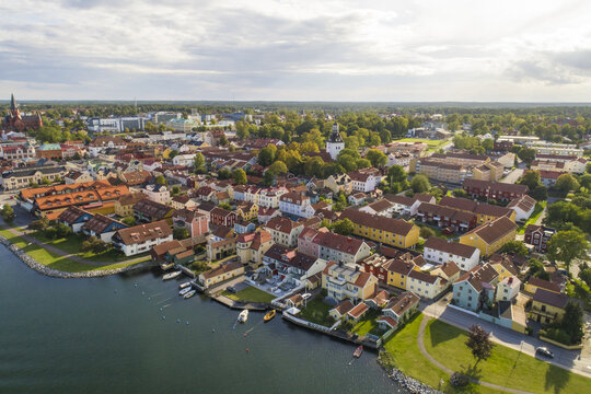 Aerial view of red-roofed buildings lining the coast, contrasting with the deep blue water and the verdant trees surrounding the church, Vastervik, Kalmar County, Sweden.