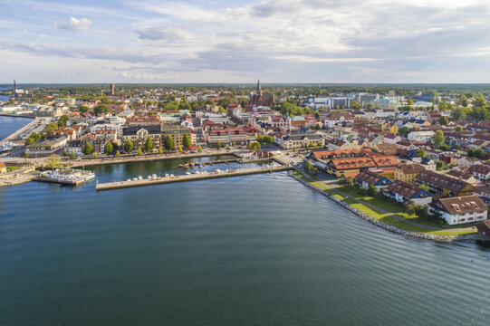 Aerial view of the serene harbor waters meet the quaint town, dominated by the spire of St. Gertrude's Church, under a vast sky, Vastervik, Kalmar County, Sweden.