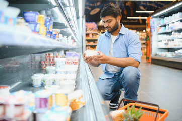 Indian man choosing dairy products in supermarket refrigerator section
