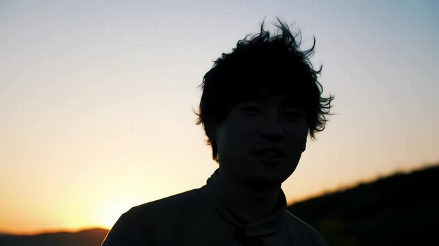 Silhouette of a young Asian man with windblown hair talking and gesturing during a beautiful golden hour sunset
