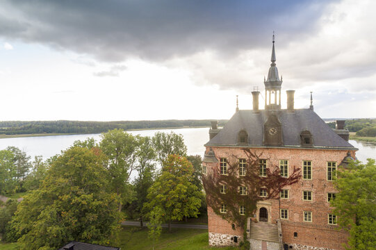 Aerial view of the historic Wiks slott with its red brick facade gently embraced by climbing vines, reflected in the serene waters, Wiks slott, Uppsala, Sweden.