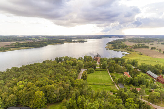 Aerial view of Wiks Castle nestled among verdant trees at the edge of Lake M&Atilde;&curren;laren under a cloudy sky, its spires reaching towards the heavens, Wiks slott, Uppsala, Sweden.