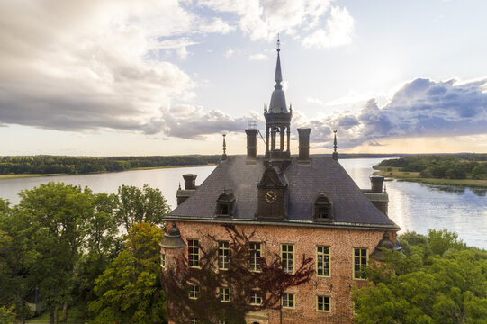 Aerial view of the majestic Wiks slott castle rising with its brick facade and dark roof against the serene lake and sky, Wiks slott, Uppsala, Sweden.