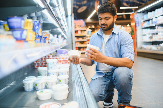 Indian man choosing yogurt in supermarket dairy section