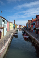 Vertical view of colorful canal with boats and tower in Burano Italy