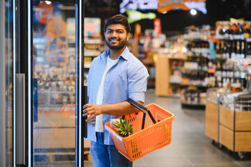 Young indian man opening refrigerator in grocery store