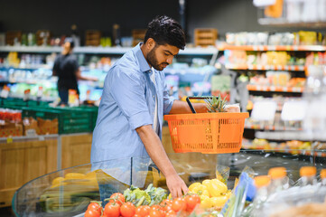 Young indian man choosing vegetables in grocery store