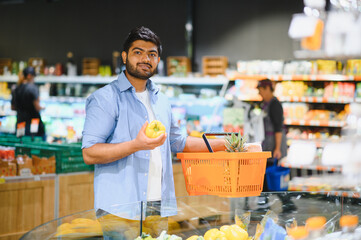 Young indian man choosing vegetables in grocery store