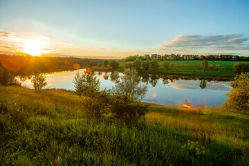 Beautiful sunset casting a brilliant golden light and lens flares over a calm lake, surrounded by...