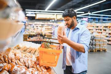Young indian man choosing bread in supermarket bakery section