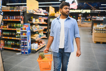Indian man shopping for groceries in supermarket with pineapple in basket