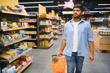 Indian customer holding shopping basket walking in supermarket