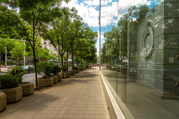ree-lined sidewalk on Kralja Milana Street – the Yugoslav Drama Theatre’s glass wall mirrors the avenue and sky, blending urban and natural beauty under Belgrade’s summer sun.