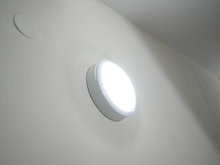 Close up of wall mounted round LED light fixture turned on in modern indoor setting with white painted surface

