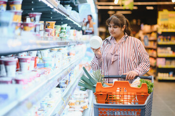 Indian woman choosing yogurt in dairy products section of supermarket