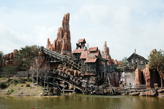 Rustic Western Theme Park Mountain with Wooden Roller Coaster and Scenic Lake View on a Bright Day