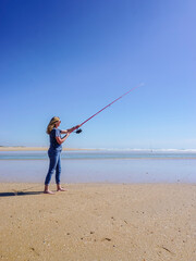 Barefoot woman on the seashore, holding a fishing rod, under a cloudless blue sky