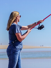 Barefoot woman on the seashore, holding a fishing rod, under a cloudless blue sky