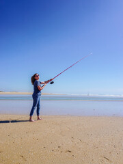 Barefoot woman on the seashore, holding a fishing rod, under a cloudless blue sky