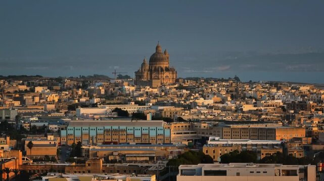 Malta, Comino island: Gozo Cathedral Church of Saint John the Baptist, Rotunda of Xewkija rising over Victoria warm toned cityscape, in golden sunset light, picturesque view of urban landscape