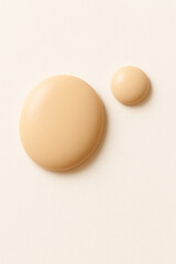 Two smooth matte beige drops of different sizes on a soft white surface. Warm tone, creamy texture, resembling skincare foundation or lotion. Minimalistic composition