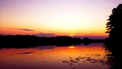 Obraz premium Beautiful sunset over tranquil lake with peaceful reflections and vibrant colors near a forested area
