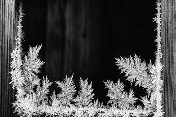 A mesmerizing black and white image of ice crystals forming fern-like patterns on a window's edges, bordering a dark background.