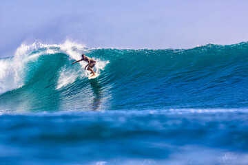 Male surfer on a blue wave at sunny day