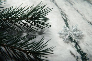 A wintry scene featuring a pine branch and a delicate, sparkling snowflake resting on a marble surface, evoking a seasonal mood.
