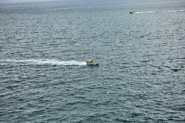Two small motorboats move across the open sea, leaving white trails behind them on the rippling water surface under a cloudy sky. boating, motion