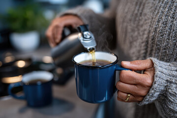 A person pours steaming tea into a blue mug, illustrating the comfort and warmth of home, displaying self-care and relaxation in a cozy environment.